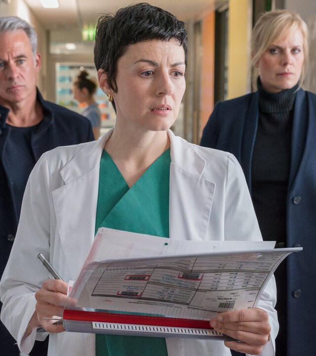 "SOKO Leipzig - In den Augen der Anderen": Jan Maybach (Marco Girnth) und Ina Zimmermann (Melanie Marschke) stehen hinter Antonia Kantor (Liza Tzschirner) in einem Krankenhausflur. Antonia Kantor trägt einen Arztkittel und hält Akten in den Händen.