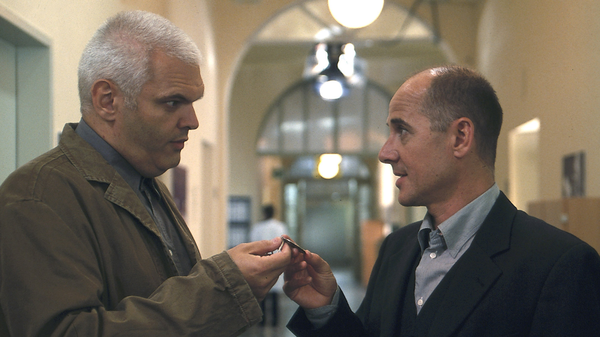 "Der letzte Zeuge - Der Fluch der verlorenen Schätze": Dr. Robert Kolmaar (Ulrich Mühe) und Peter Lawin (Lázló I. Kish) unterhalten sich im Flur. Lawin gibt Dr. Kolmaar ein Amulett.