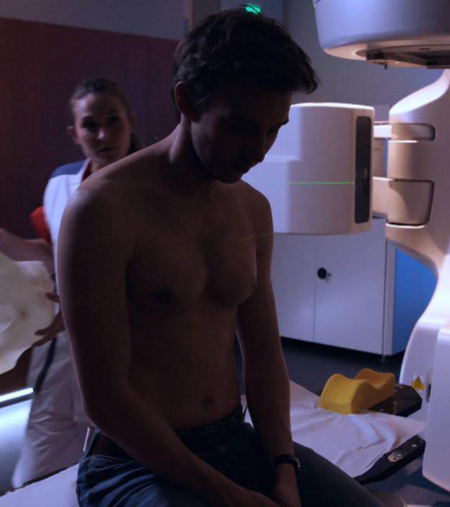 "Sense of Tumour - Stadium 1": Tristan (Maarten Nulens) sitzt trübselig auf der Liege einer medizinischen Maschine, während eine Krankenschwester eine Maske für ihn vorbereitet.