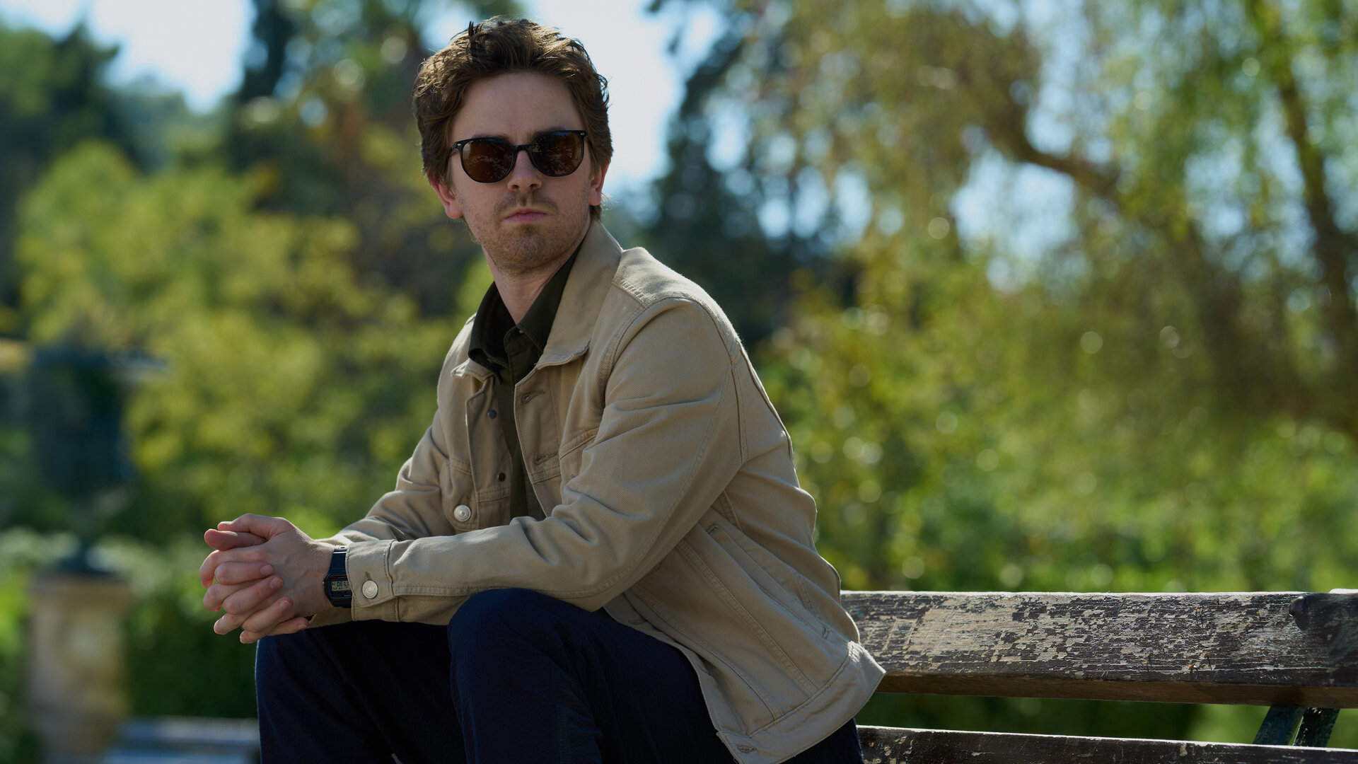 "The Assassin - Eine feurige Pizza": Edward (Freddie Highmore) sitzt im Freien auf einer Bank. Er trägt eine Sonnenbrille und beobachtet etwas.