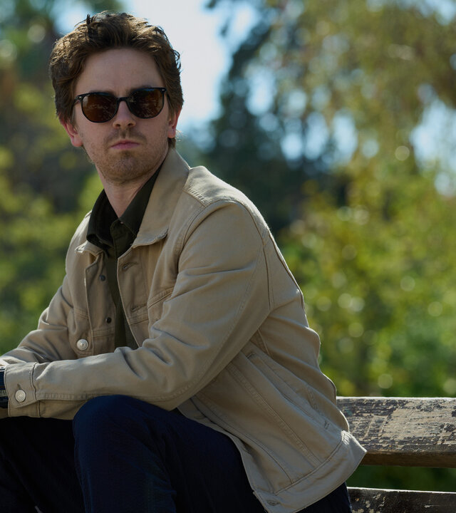 "The Assassin - Eine feurige Pizza": Edward (Freddie Highmore) sitzt im Freien auf einer Bank. Er trägt eine Sonnenbrille und beobachtet etwas.