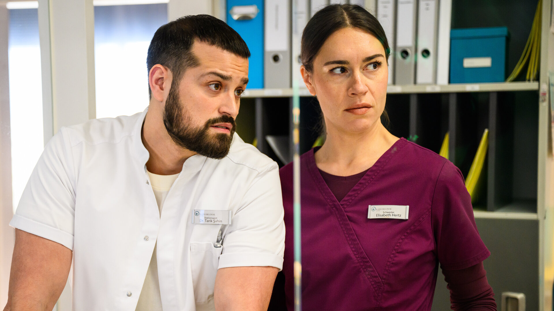 "Bettys Diagnose - In den Sternen": Tarik (Nicolas Fethi Türksever) und Betty (Henrike Hahn) stehen nebeneinander und schauen in die gleiche Richtung. Im Hintergrund steht ein Aktenschrank.