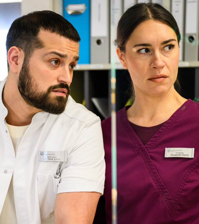 "Bettys Diagnose - In den Sternen": Tarik (Nicolas Fethi Türksever) und Betty (Henrike Hahn) stehen nebeneinander und schauen in die gleiche Richtung. Im Hintergrund steht ein Aktenschrank.