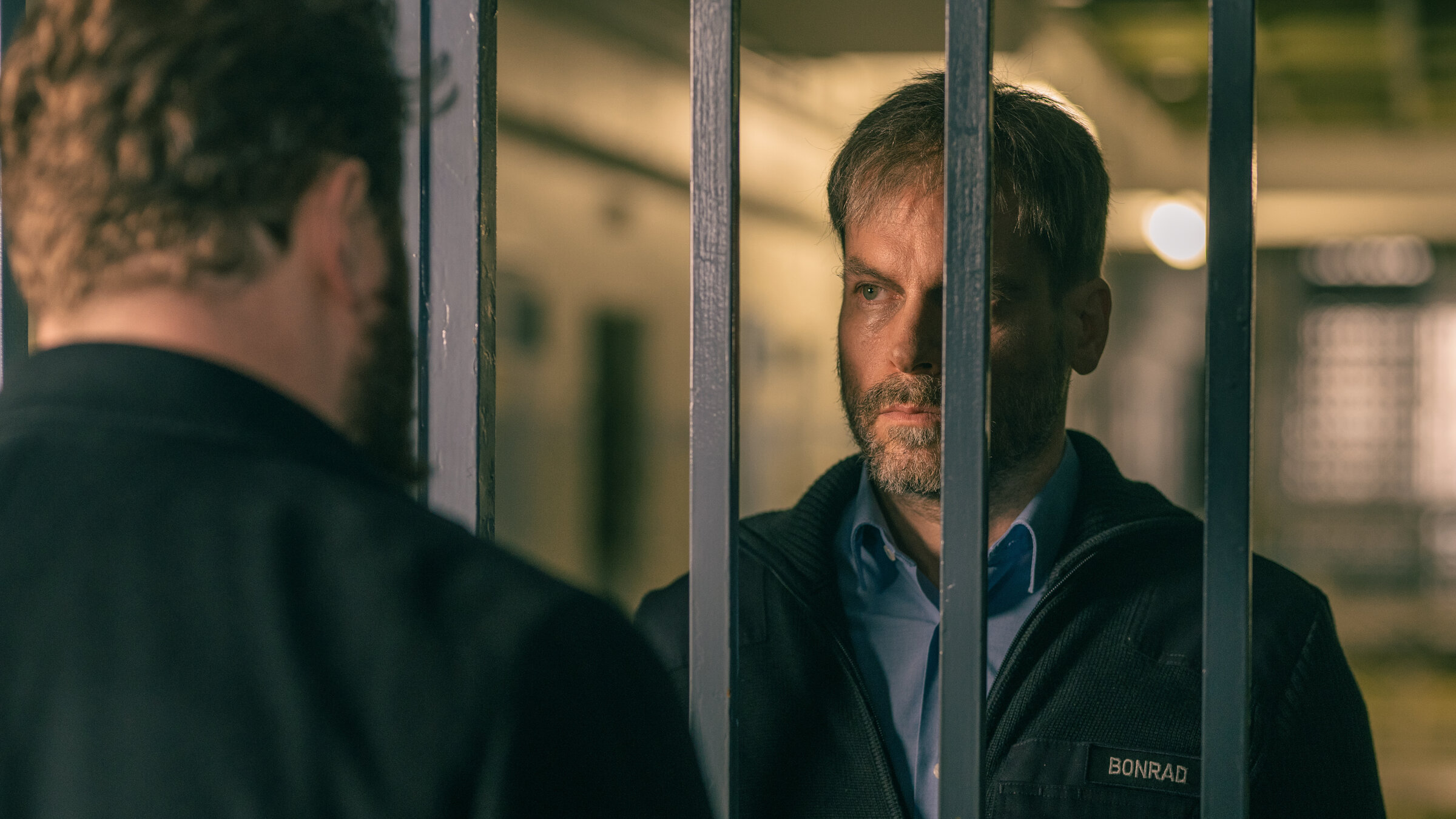 "Ein Fall für zwei - Entzweit": Leo Oswald (Wanja Mues) steht hinter einer vergitterten Tür in der JVA. Er schaut Benjamin Hornberg (Antoine Monot) durch die Gitterstäbe ernst an. Benjamin Hornberg steht mit dem Rücken zur Kamera.