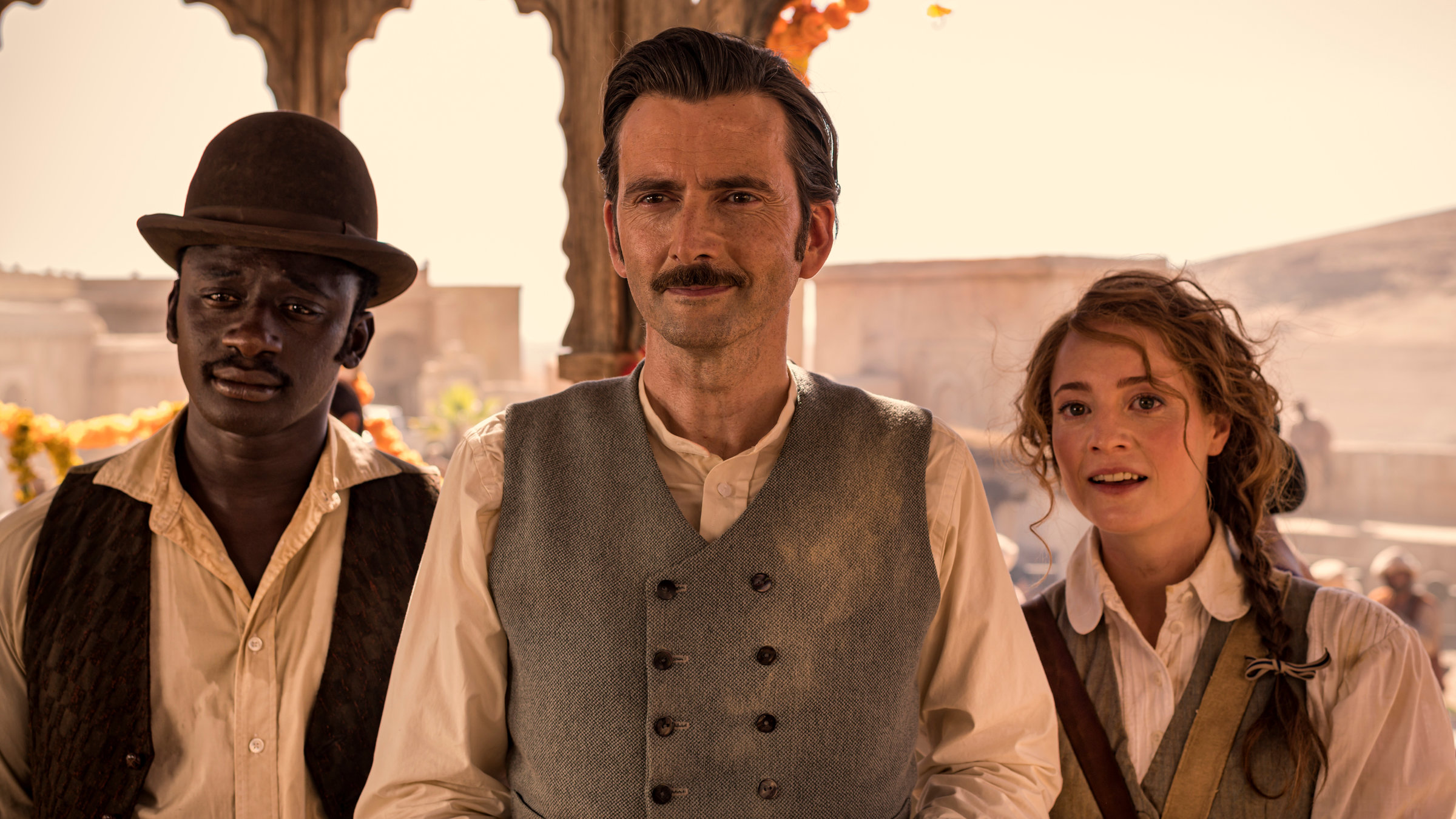 "In 80 Tagen um die Welt (4)": Phileas Fogg (David Tennant), Abigail Fix (Leonie Benesch) und Passepartout (Ibrahim Koma) stehen nebeneinander unter dem Dach eines indischen Pavillons.