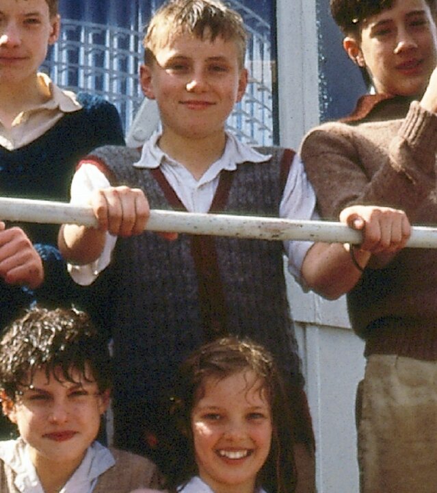 "Fünf Freunde auf dem Leuchtturm": Julian (Marco Williamson), George (Jemima Rooper), Dick (Paul Child), Anne (Laura Petela) und Tinker (James Tomlinson) lächeln zufrieden hinter einem Geländer auf einem Leuchtturm. Während Julian einen Glockenschläger in den Händen hält, ruht Tinkers Hand auf der Oberfläche der Glocke.
