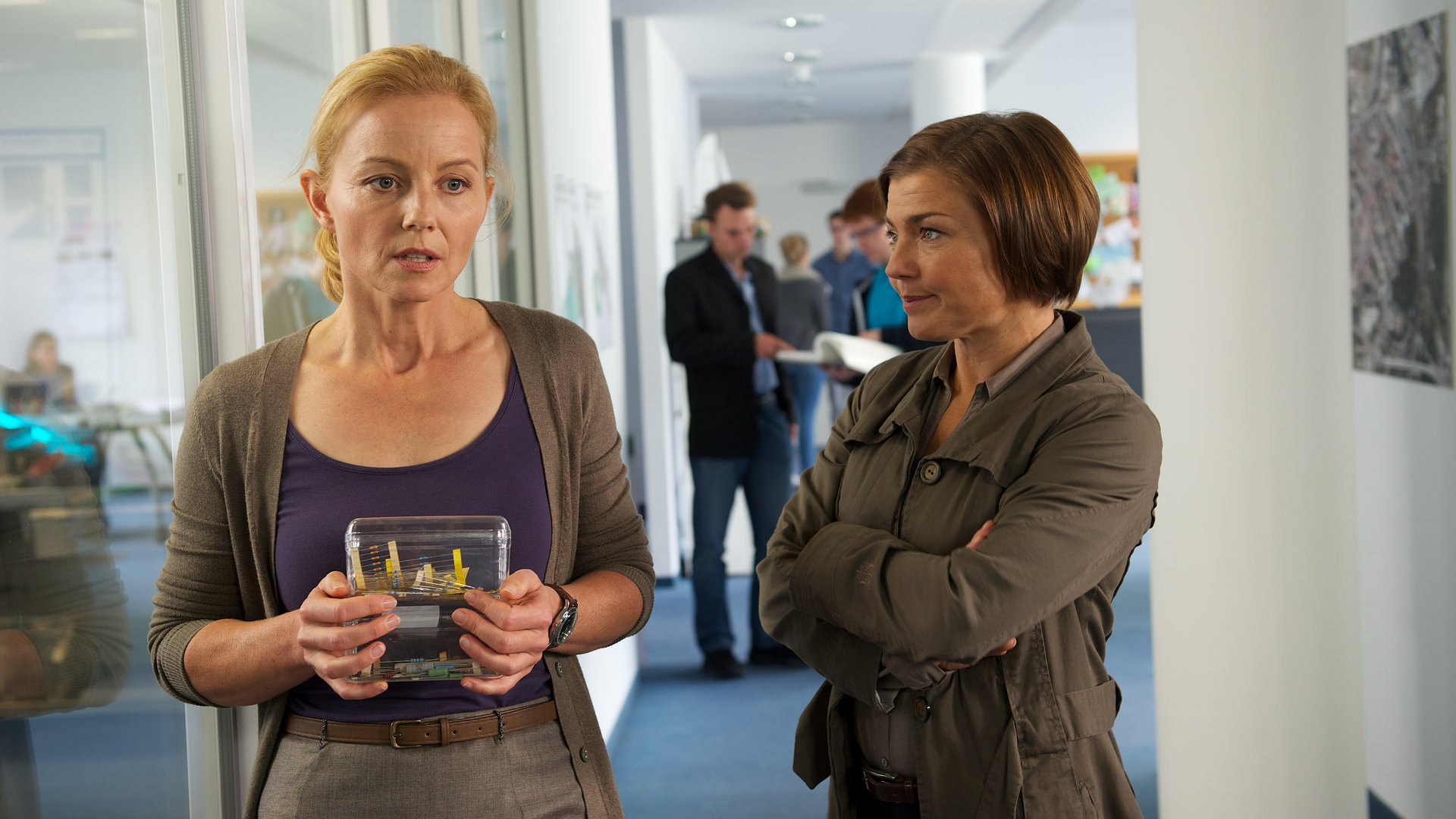 "SOKO Wismar - Der letzte Aufguss": Melanie Meyer (Carina Wiese) steht in einem Flur bei Katrin Börensen (Claudia Schmutzler) und ist sichtlich angespannt. Katrin Börensen hat die Hände vor der Brust verschränkt und schaut Melanie an.
