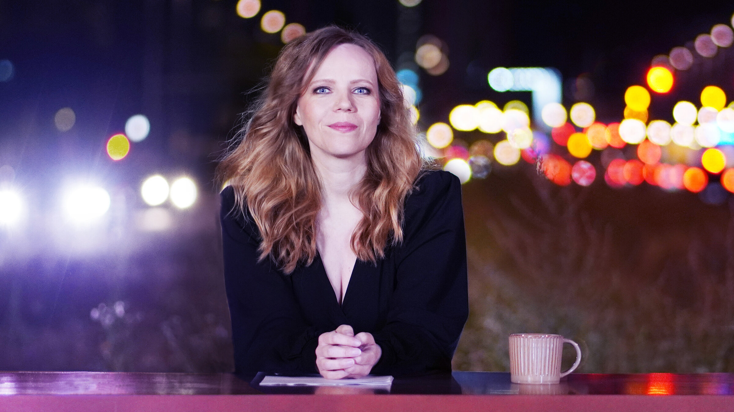 "Bosetti Late Night": Sarah Bosetti sitzt hinter einem pinkfarbenen Tresen. Sie schaut freundlich in die Kamera. Neben Ihr steht eine rosafarbene Kaffeetasse.