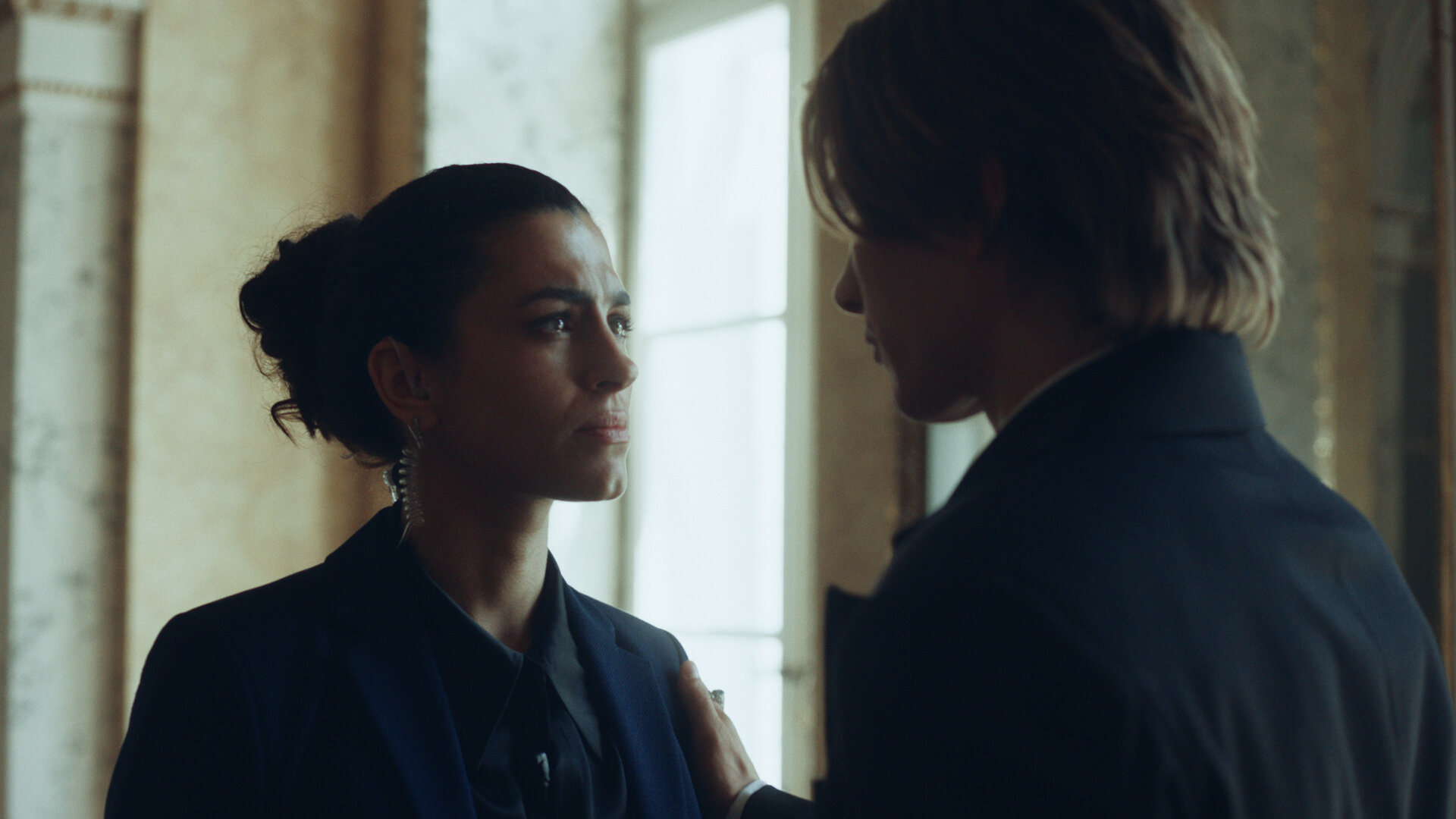 "Crystal Wall - Begehren": Nicolas Dardenne (Gustav Schmidt) berührt Louna Lloris (Anna Bardavelidze) an ihrer linken Schulter. Beide stehen in einem hellen Raum und schauen sich in die Augen.