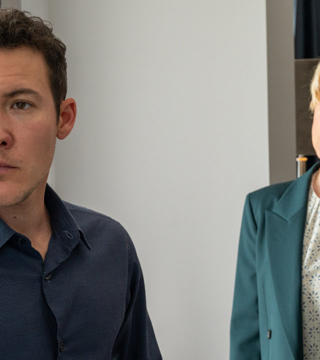 "SOKO Stuttgart - Was geschah mit Rabea K.?": In einem Hotelzimmer schaut Robert Henschel (Brix Schaumburg) mit eisernem Blick ins Leere, während er von Kriminalhauptkommissarin Martina Seiffert (Astrid M. Fünderich) mit Argusaugen kritisch beobachtet wird.
