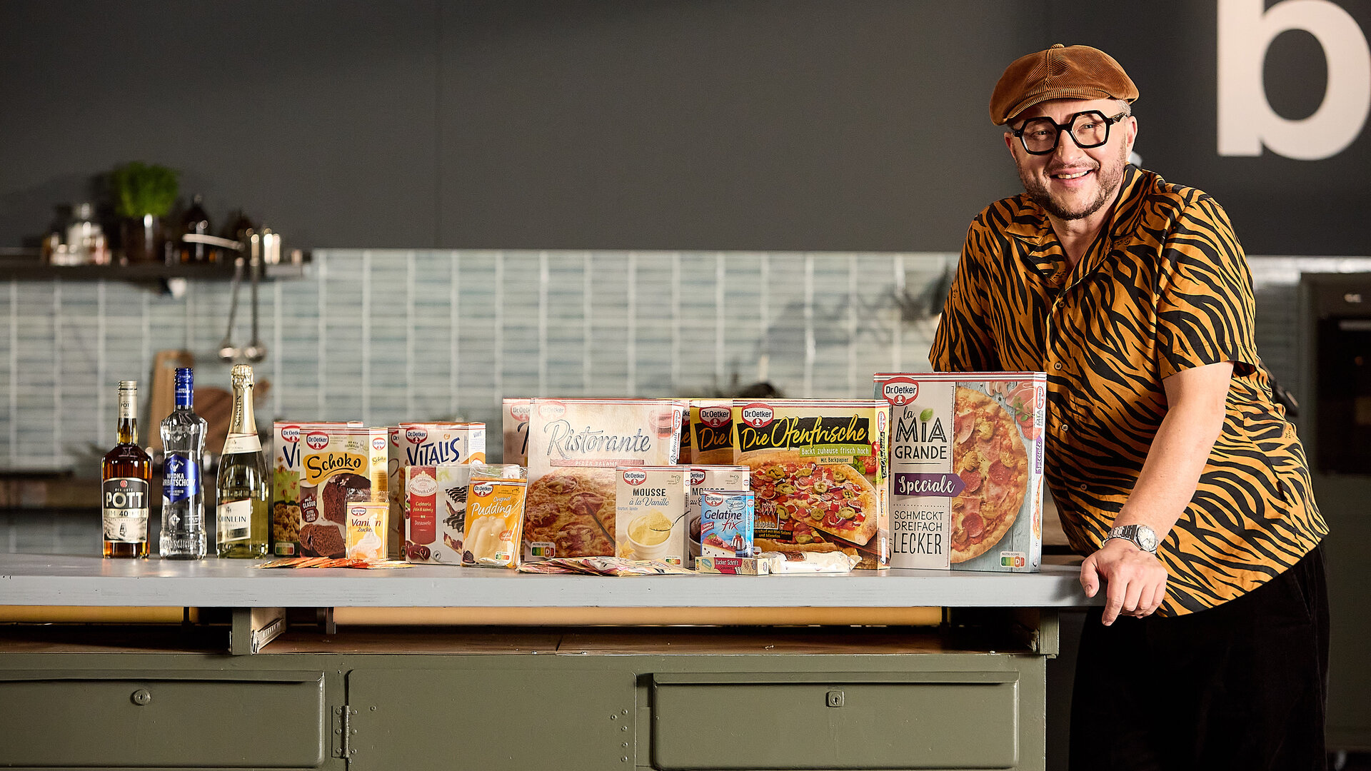 "besseresser: Die Wahrheit über Dr. Oetker- Food Stories mit Sebastian Lege": Sebastian steht am Tresen seiner Werkstattküche. Die Arbeitsfläche ist gefüllt mit Produkten von Dr. Oetker.