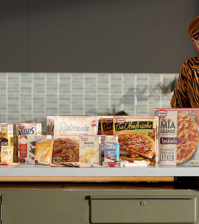 "besseresser: Die Wahrheit über Dr. Oetker- Food Stories mit Sebastian Lege": Sebastian steht am Tresen seiner Werkstattküche. Die Arbeitsfläche ist gefüllt mit Produkten von Dr. Oetker.