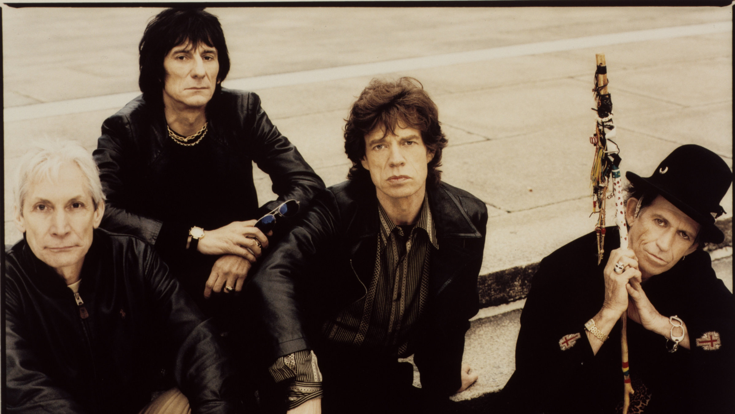 "The Rolling Stones: Voodoo Lounge": Die Bandmitglieder der Rolling Stones sitzen auf zwei Treppenstufen, alle schwarz gekleidet und blicken mit ernsten Gesichtern hoch in die Kamera.