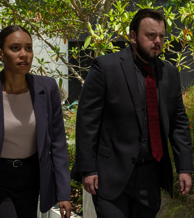 "North Shore – Tod in Sydney – Sophies Laptop": DS Meg Driscoll (Kirsty Sturgess) und DS Max Drummond (John Bradley) gehen nebeneinander durch ein Wohngebiet. Meg trägt eine blaue Dokumentenmappe.