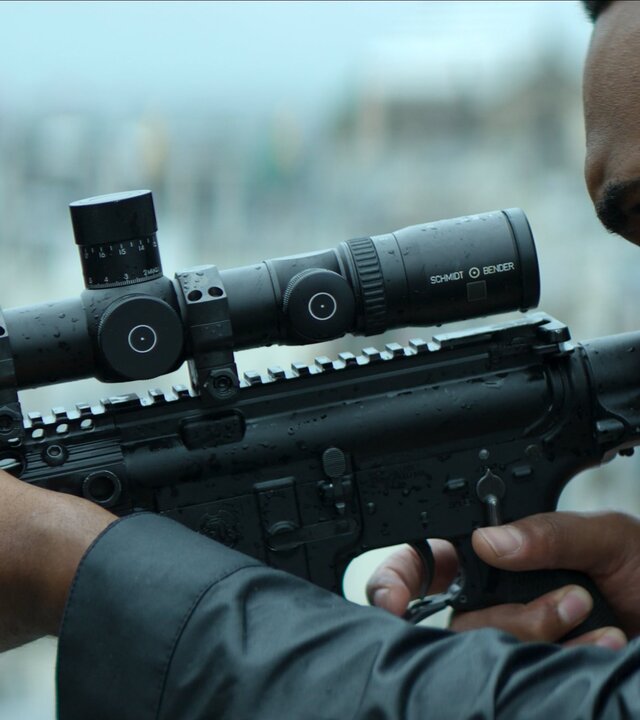 "Paris Has Fallen - Der Scharfschütze": Matthew (Tyler Fayose) hält ein angelegtes Präzisionsgewehr mit Zielfernrohr in den Händen. Sein rechter Zeigefinger geht zum Abzug. Er befindet sich offenbar auf einem Dach. Im Hintergrund sind unscharf zahlreiche Gebäude zu sehen.