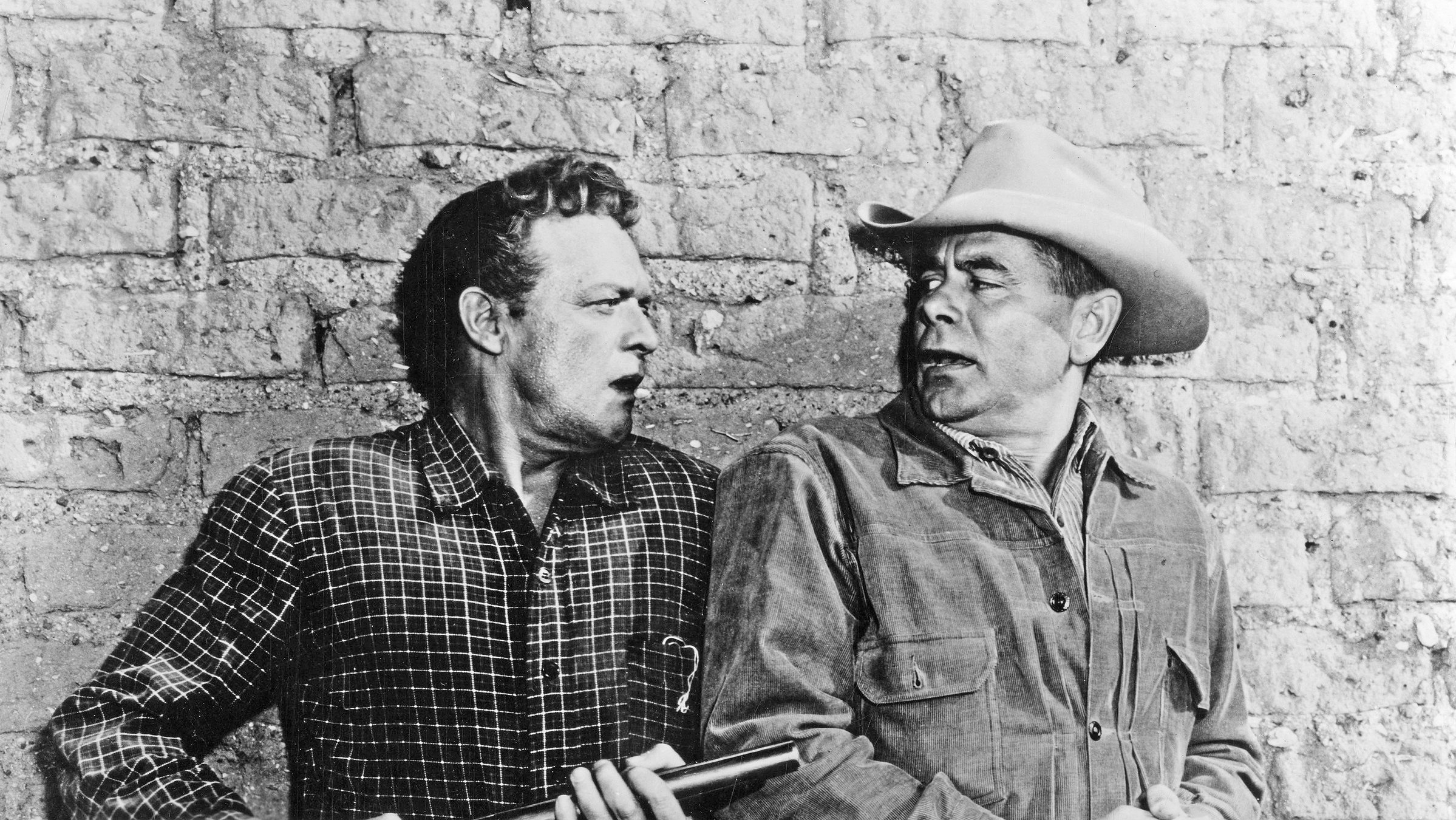 "Zähl bis drei und bete": Mit angespannten Gesichtern und ganz nah beieinander stehen Dan Evans (Van Heflin) und Ben Wade (Glenn Ford) dicht an eine Backsteinwand gepresst. Wade dreht sich über die Schulter blickend zu Evans um, der eine abgesägte Schrotflinte auf ihn richtet.