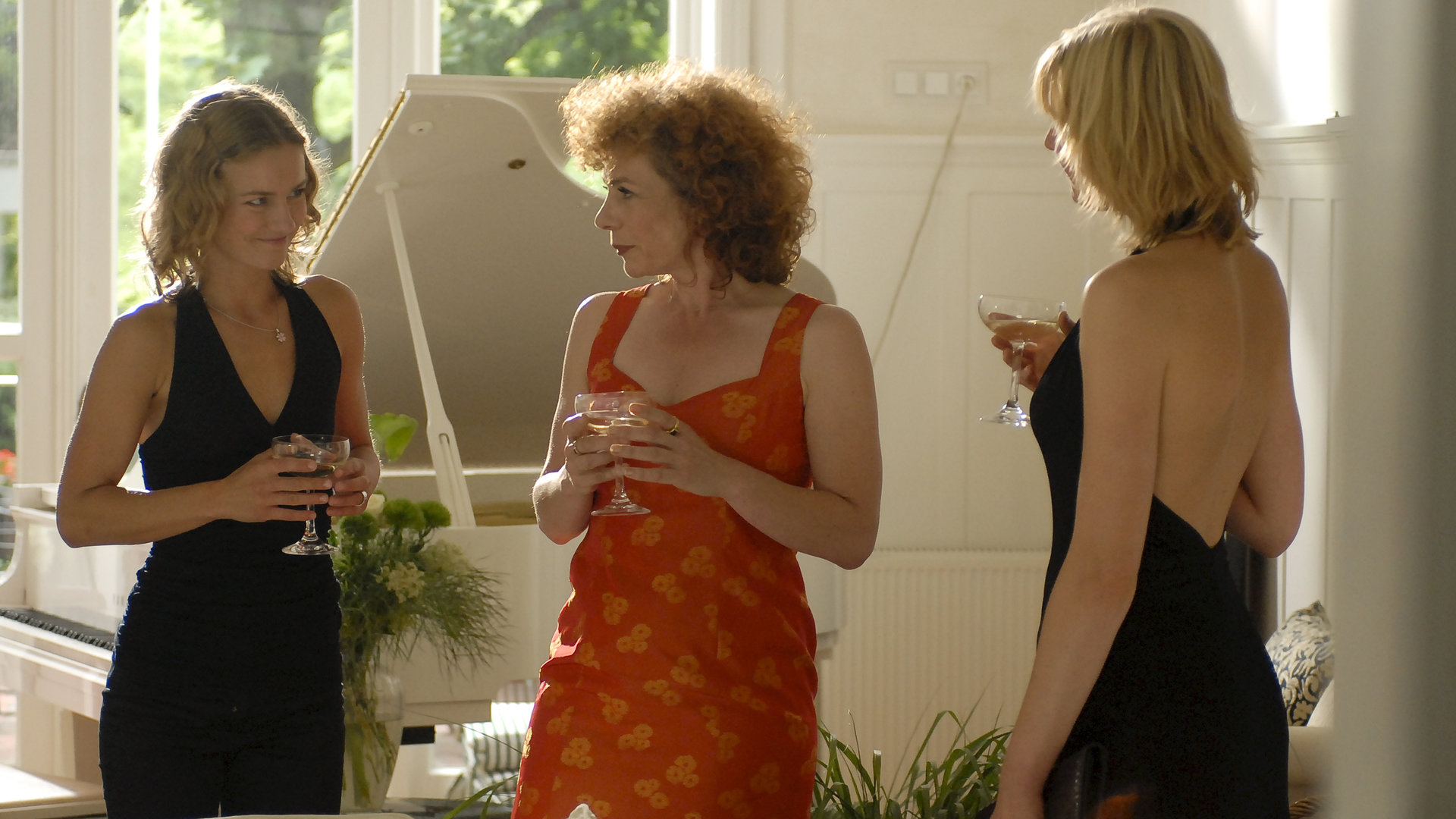 "Notruf Hafenkante - Herzenssache": Melanie (Sanna Englund), Vera Gonscharow (Nina Hoger) und Franzi (Rhea Harder) stehen schick gekleidet, mit Cocktails in der Hand, beisammen und unterhalten sich. Im Hintergrund steht ein weißer Flügel.