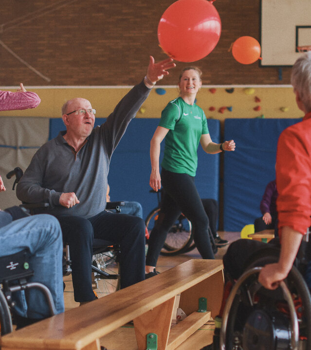 "Aktion Mensch - Glückszahlen der Woche": in einer Sporthalle sind mehrere Menschen versammelt und spielen mit einem roten Ball. Einige sitzen in Rollstühlen.