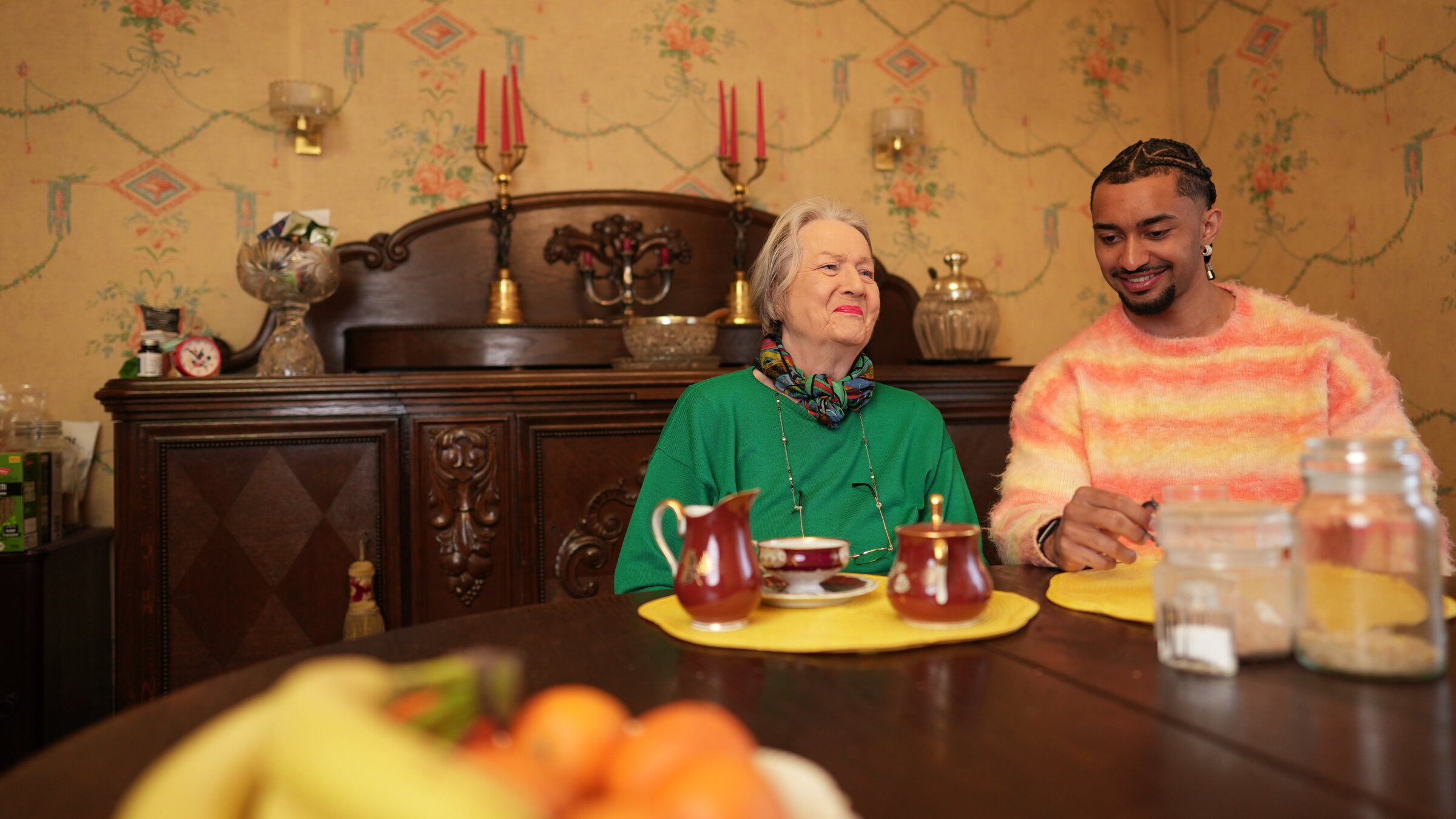 "37°Leben: WG mit Oma. Zwischen Fürsorge, Uni und Start-up": Eva (81) und Louis (26) sitzen an einem Tisch. Im Hintergrund steht eine antike Anrichte.