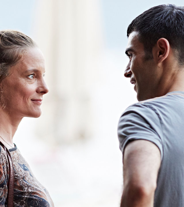 "Es gilt das gesprochene Wort": Marion (Anne Ratte-Polle) und Baran (Ogulcan Arman Uslu) stehen sich gegenüber und lächeln sich an. Im Hintergrund ist ein türkischer Urlaubsort zu erahnen.