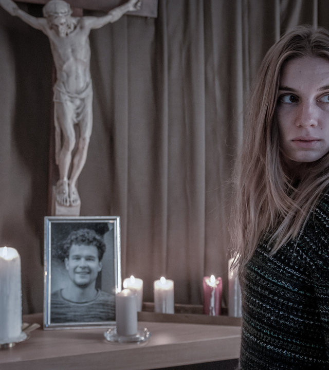 "SOKO Linz - Lazarus": Clara (Maya Unger) steht vor dem Altar ihres Bruders Philipps, auf dem ein Porträt von ihm und leuchtende Kerzen stehen. Über dem Altar hängt eine Statue von Jesus am Kreuz.