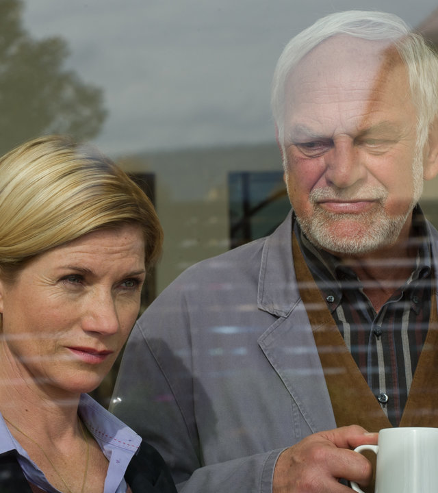 "SOKO Stuttgart - Shopping-Queen": Martina Seiffert (Astrid M. Fünderich) und Friedemann Sonntag (Christian Pätzold) stehen an einem Fenster. Friedemann hält einen weißen Porzellanbecher in der Hand und schaut Martina besorgt an. Sie hat den Blick von ihm abgewandt und sieht nach draußen.