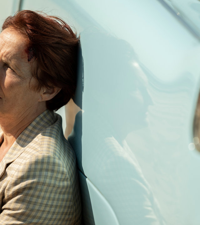 "Killing Eve - Es ist eine Qual und ich bin ausgehungert": Carolyn (Fiona Shaw) sitzt angelehnt an ein blaues Auto an einem Strand und schaut erschöpft nach vorne.