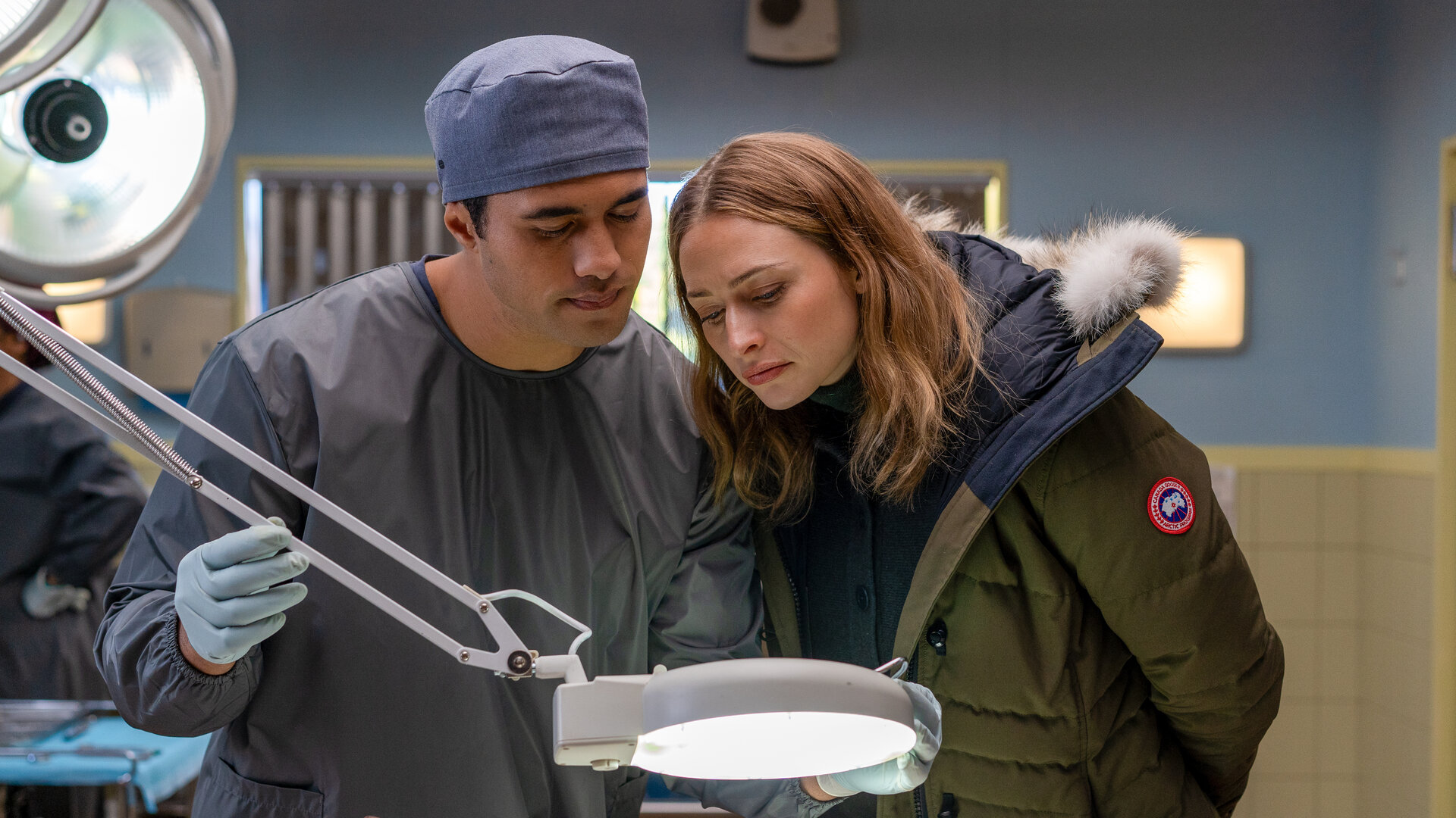 "Queenstown Murders – Zum Sterben schön - Ein explosives Geheimnis": Dr. Ihaka Cooper (Alex Tarrant) und Detective Sergeant Anais Mallory (Chelsie Preston Crayford) stehen eng beieinander an einem Seziertisch. Sie blicken auf einen abgetrennten Arm, der vor ihnen liegt.
