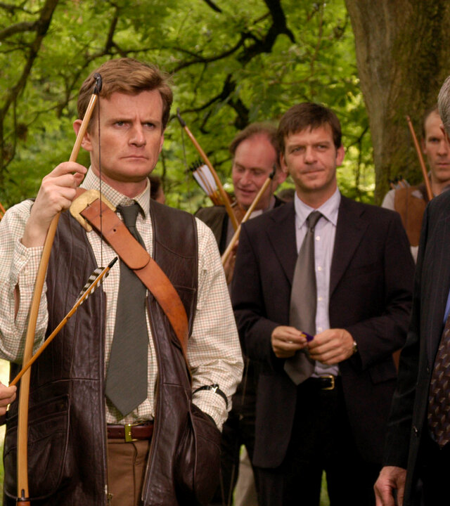 "Inspector Barnaby - Ganz in Rot": Robin Lawson (Martin Wenner), und Ned Fitzroy (Charles Edwards) mit Pfeil und Bogen in den Händen stehen zusammenmit DS Ben Jones (Jason Hughes) und DCI Tom Barnaby (John Nettles) unter einem Baum und schauen in eine Richtung. Hinter ihnen stehen noch weitere Männer.