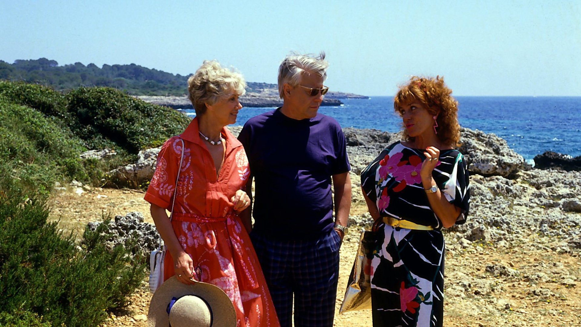 "Die Wicherts von nebenan: Spanische Zeiten": Hannelore (Maria Sebaldt) und Eberhard (Stephan Orlac) stehen neben Frau Lallinger (Gabi Gasser) und blicken sie fragend an. Im Hintergrund ist das Meer zu sehen.