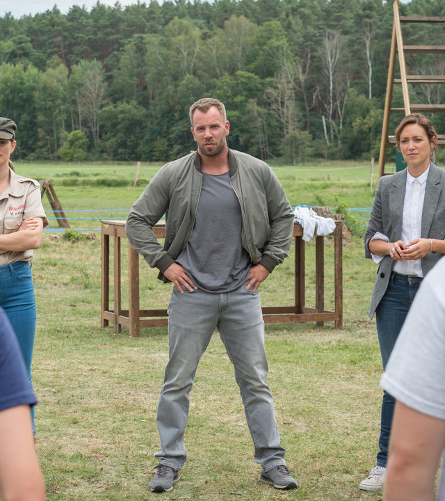 "SOKO Wismar – Zucht und Ordnung": Im Hintergrund sind Geräte für den Hindernislauf des Bootcamps zu sehen. Davor stehen Verhaltenstherapeutin Veronika Frisch (Alexandra Gottschlich), Lars Pöhlmann (Dominic Boeer) und Karoline Joost (Nike Fuhrmann). Diese blicken auf zwei Jugendliche im Bootcamp-Outfit, die mit dem Rücken zur Kamera stehen.