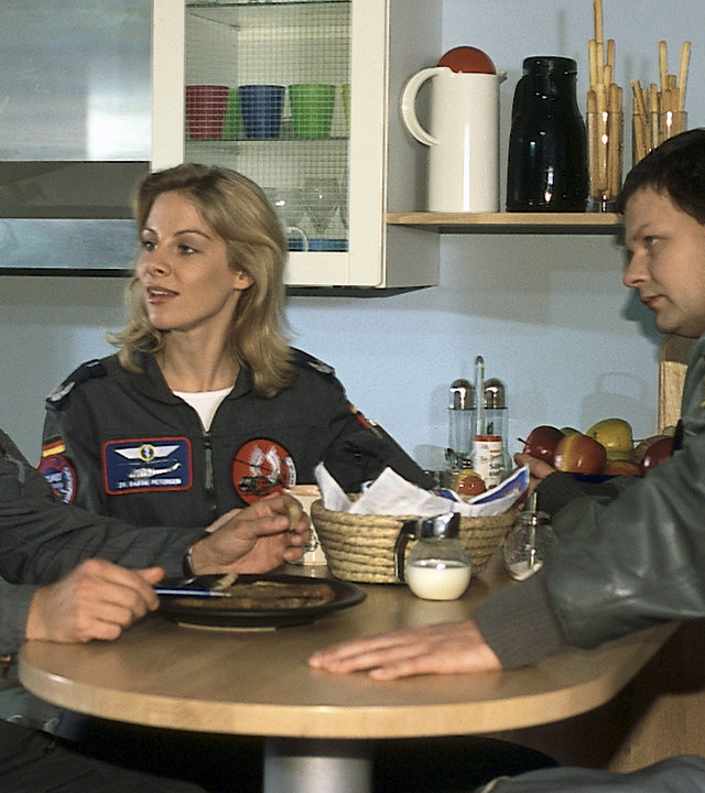 "Die Rettungsflieger - Zum Dessert": Dr. Sabine Petersen (Marlene Marlow) sitzt zwischen Alex (Matthias Leja), Thomas (Ulrich Bähnk) und Wollcke (Oliver Hörner) am gedeckten Bar-Tisch in der Küche. Sabine und Alex sehen sich intensiv an, Thomas und Wollcke beobachten die beiden.