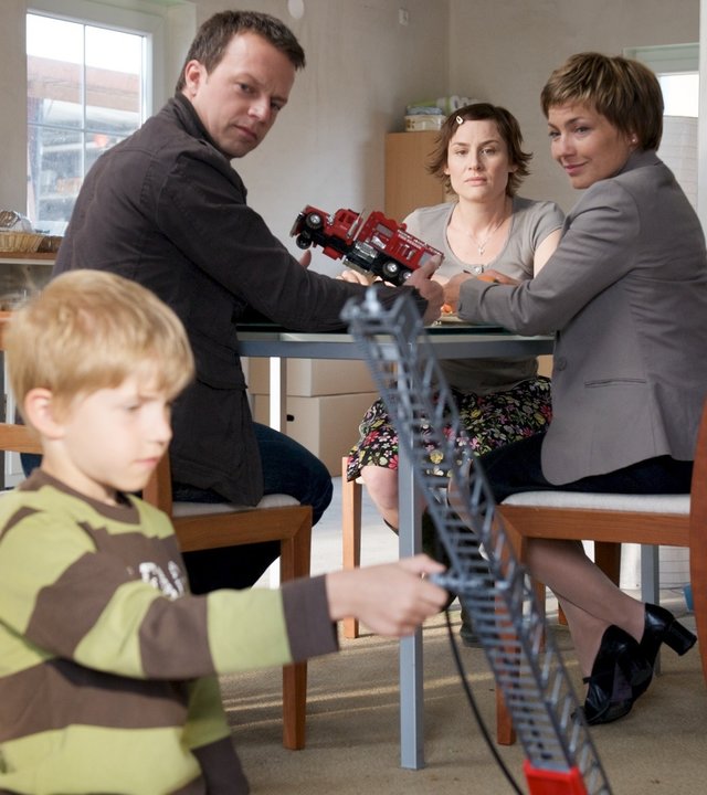 "SOKO Wismar - Eigenheim": An einem Küchentisch sitzen Sven Herzog (Michael Härle), Doreen Scheurich (Daniela Holtz) und Katrin Börensen (Claudia Schmutzler). Tobias (Eric Wüst) spielt mit einem Feuerwehrauto vor dem Tisch auf dem Boden.