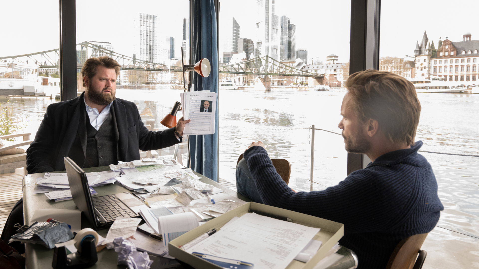 "Ein Fall für zwei - Kanalratten": Benni Hornberg (Antoine Monot, Jr.) und Leo Oswald (Wanja Mues) sitzen im Hausboot und sprechen mit einander. Benni zeigt dabei Leo eine Akte.