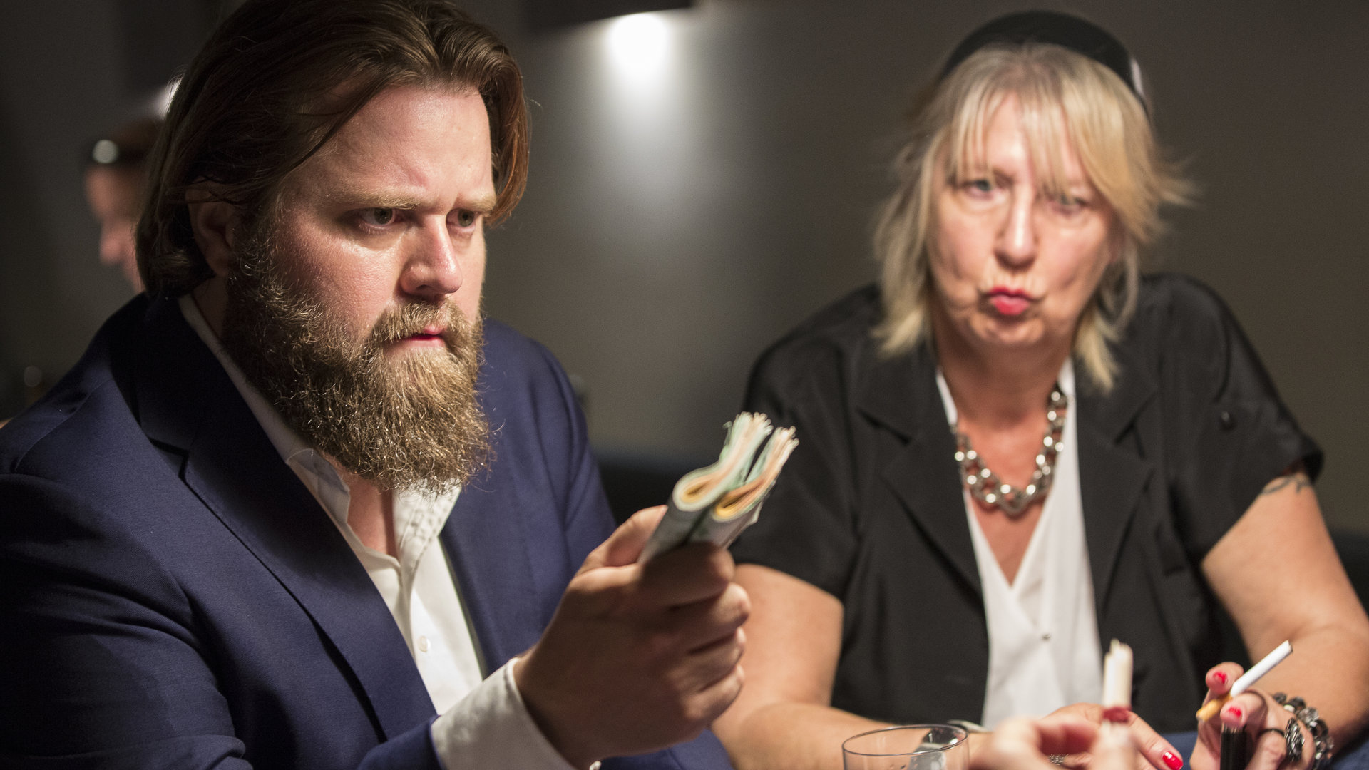"Ein Fall für zwei – Das Apartment": Strafverteidiger Benni Hornberg (Antoine Monot, Jr.) sitzt rechts neben einer Frau an einem Tisch und bietet demjenigen, der sich ihm gegenüber befindet, mit ernstem Blick ein Bündel Geld an.