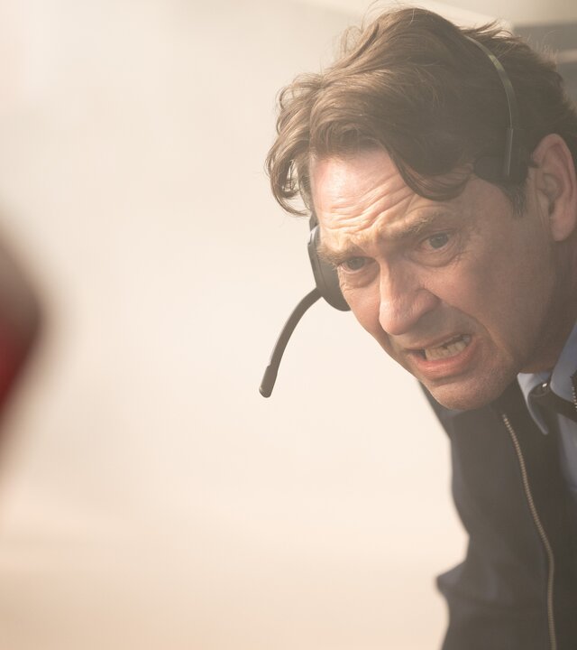 "Vigil - Tödliche Drohnen: Attacke": Air Marshal Marcus Grainger (Dougray Scott) duckt sich panisch und erschrocken nach unten weg. Er trägt ein Head-Set.