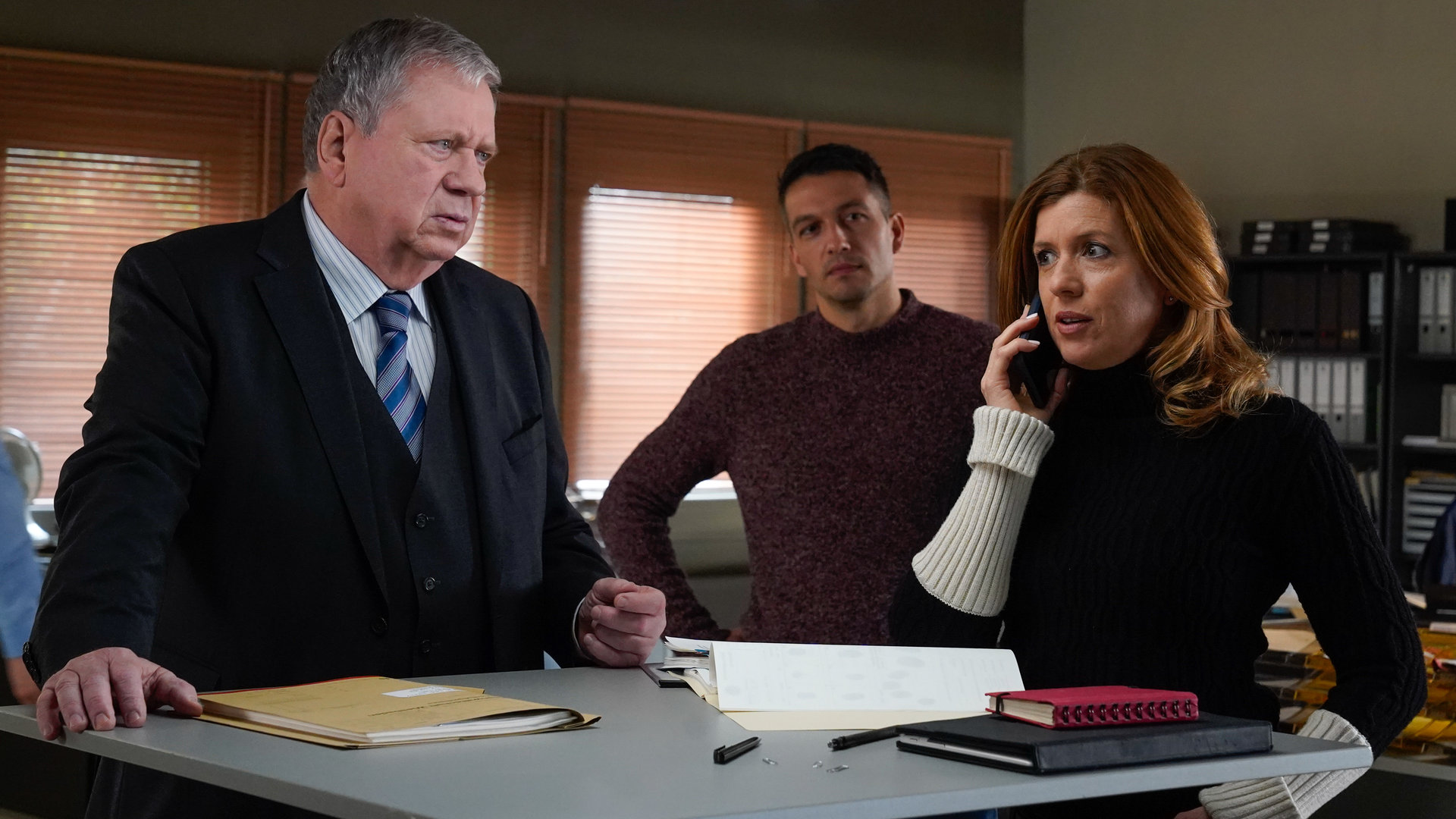 "Der Staatsanwalt - Tödliches Erbe": Oberstaatsanwalt Bernd Reuther (Rainer Hunold) steht mit Hauptkommissarin Kerstin Klar (Fiona Coors) an einem Besprechungstisch. Kerstin Klar telefoniert, während Oberkommissar Max Fischer (Max Hemmersdorfer) aus dem Hintergrund zusieht.