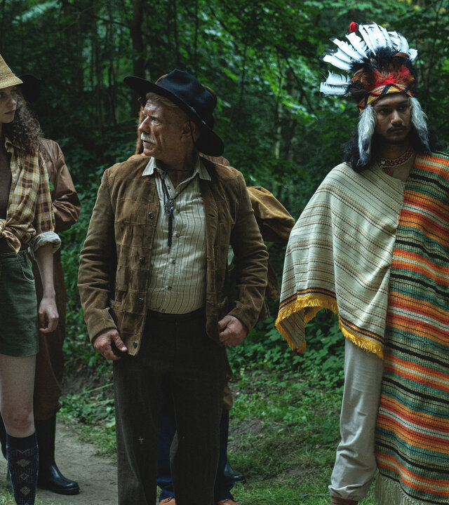 "We're on it, comrades! - Die Ballade vom Ziegenmonster": Hora (Leoš Noha), Dr. Pavlas (Ján Jackuliak), Eva (Darija Pavlovičová), Čurko (Richard Stanke), Shushrut (Kampan Soni) stehen im Wald auf einem Pfad und schauen zu "Deputy" (Saša Rašilov), der ihnen gegenüber steht.
