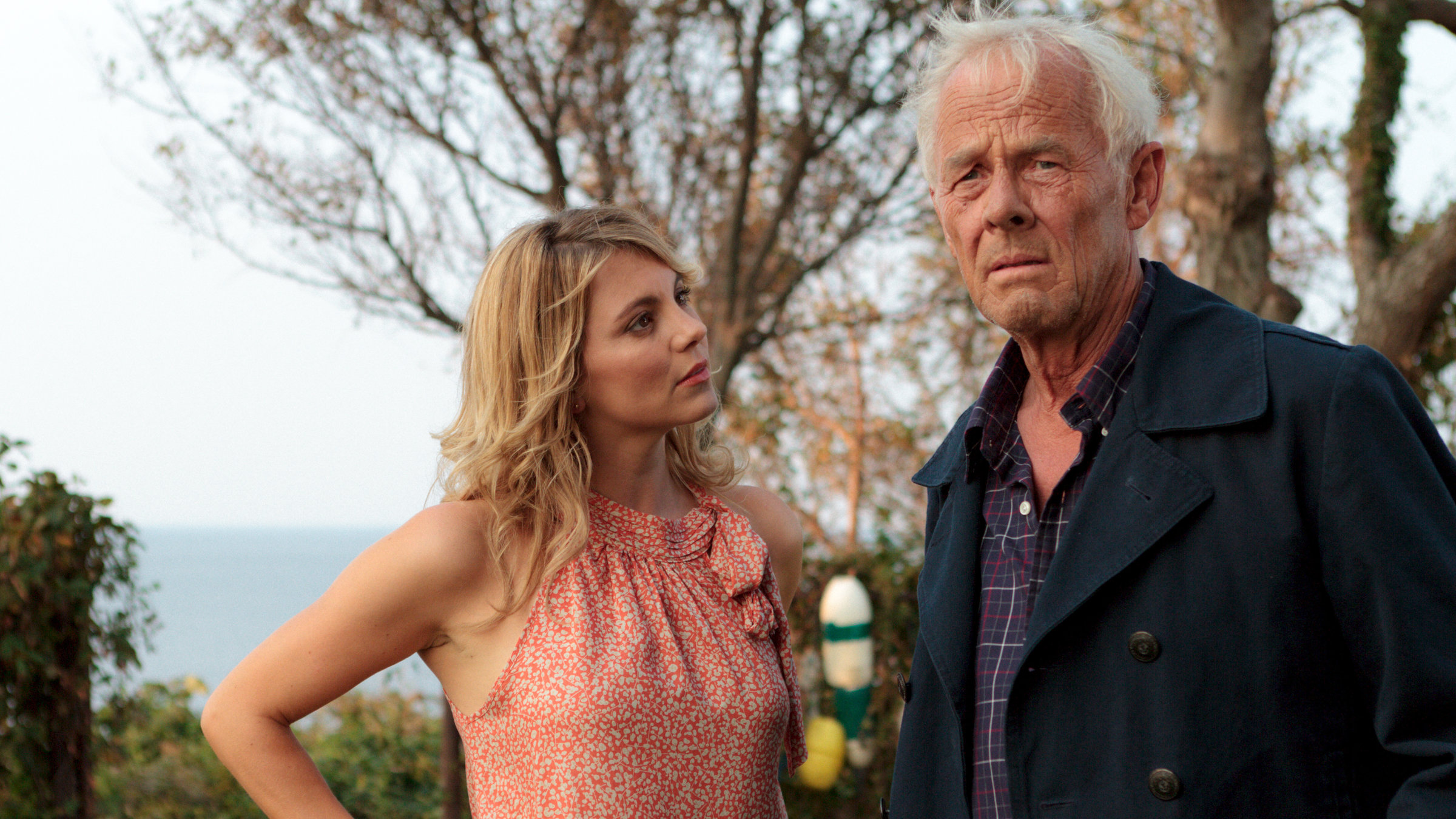 "Katie Fforde: Leuchtturm mit Aussicht": Anna Wilcox (Luise Bähr) und Joshua Hasley (Rolf Becker) stehen zusammen in einem Garten und unterhalten sich. Im Hintergrund sieht man das Meer.