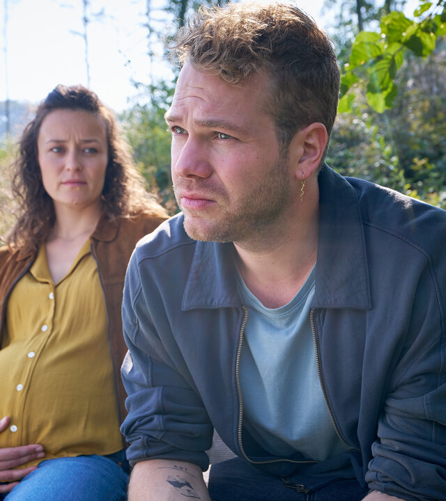 "Like A Loser: Ernster gehts nicht": Marie (Tinka Fürst) sitzt mit ihrem Babybauch auf einer Parkbank und blickt besorgt zu Julian (Ben Münchow), der mit angespannter Miene nachdenklich in die Ferne schaut.