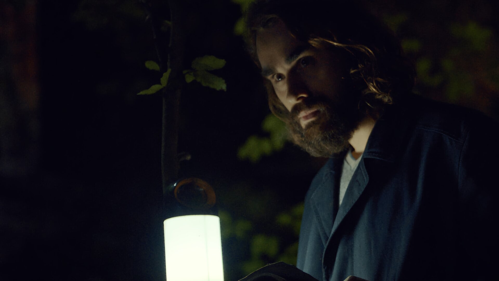 "Moresnet - The Book of Death: Das Tagebuch": Ben Schotz (Boris Van Severen) steht nachts in einem Wald. In seiner linken Hand hält er ein aufgeschlagenes Tagebuch, das er mit einer elektrischen Laterne beleuchtet, die er in seiner rechten Hand hält. Die Szene wirkt durch den fahlen Lichtschein gespenstisch.