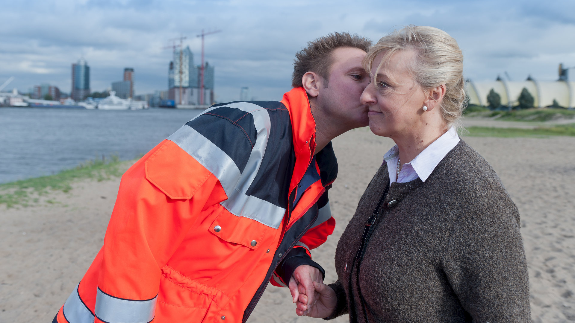 "Notruf Hafenkante - Mäggy und der göttliche Plan": Dr. Haase (Fabian Harloff) steht neben Mäggy (Johanna Bittenbinder) am Hafen. Er hält ihre Hand und gibt ihr ein Küsschen auf die Wange.