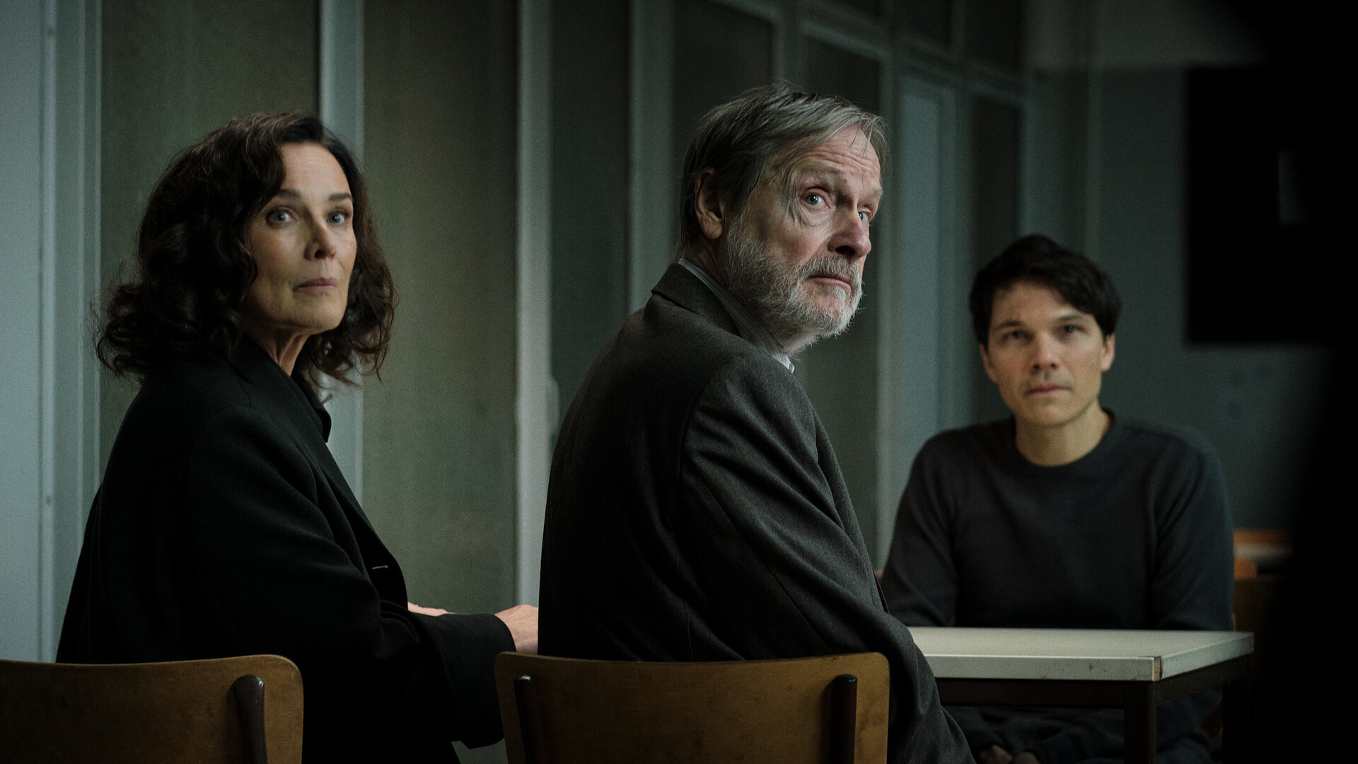 "Ein Fall für Conti – Der verlorene Sohn": Anna Conti (Désirée Nosbusch) und Friedrich Klopfer (Michael Wittenborn) sitzen auf der einen Seite eines Tisches, Falk Klopfer (Sebastian Urzendowsky) auf der anderen. Sie befinden sich im eintönigen Besuchsraum eines Gefängnisses. Conti und Friedrich sind von Falk abgewandt, alle drei schauen in dieselbe Richtung.