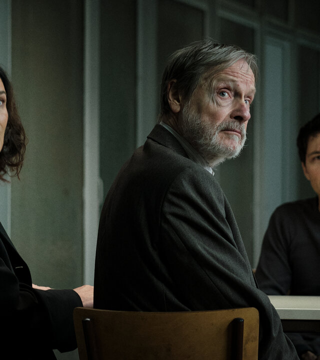 "Ein Fall für Conti – Der verlorene Sohn": Anna Conti (Désirée Nosbusch) und Friedrich Klopfer (Michael Wittenborn) sitzen auf der einen Seite eines Tisches, Falk Klopfer (Sebastian Urzendowsky) auf der anderen. Sie befinden sich im eintönigen Besuchsraum eines Gefängnisses. Conti und Friedrich sind von Falk abgewandt, alle drei schauen in dieselbe Richtung.