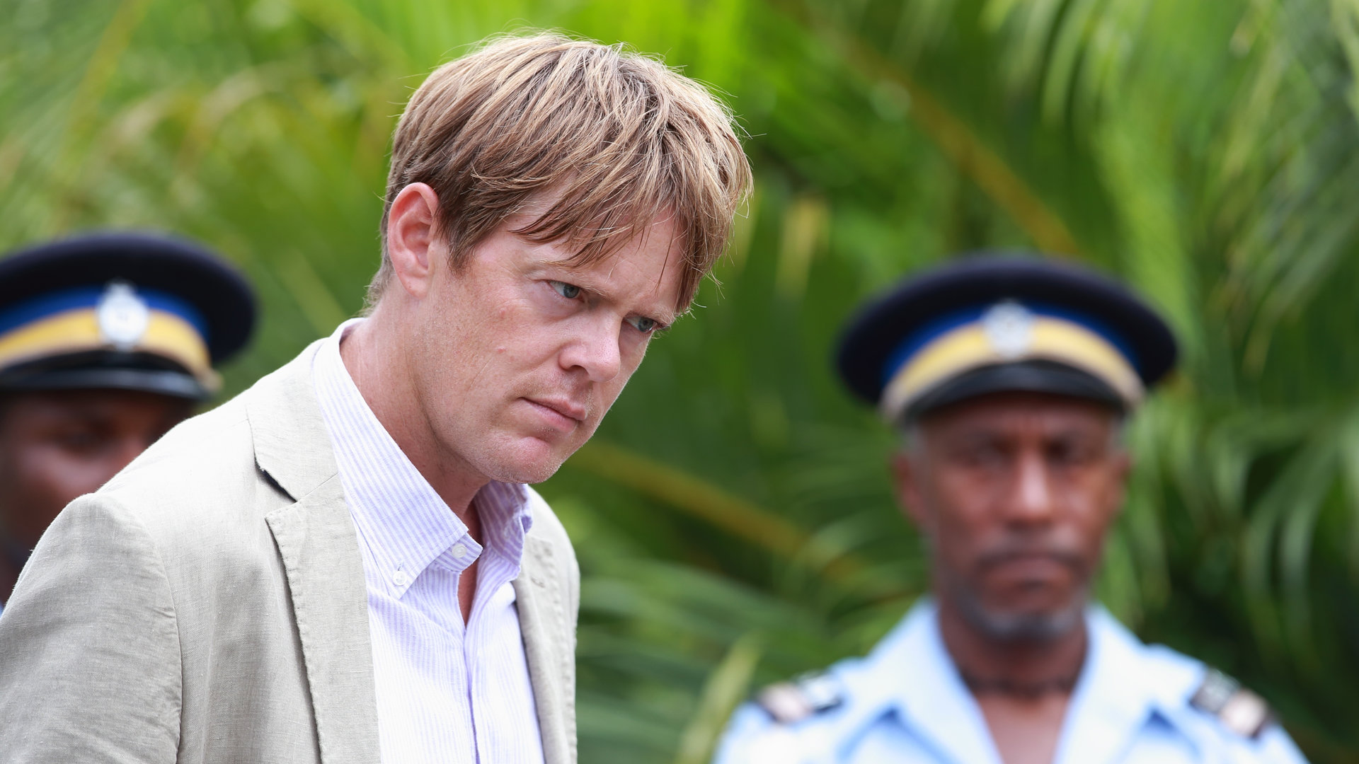 "Death in Paradise - Doppelmord der anderen Art": Humphrey (Kris Marshall) in Nahaufnahme. Hinter ihm stehen zwei Polizisten.