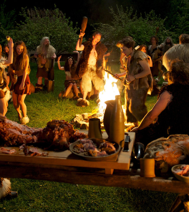 "SOKO Wismar - Neandertal ist überall": Um ein Lagerfeuer herum stehen viele Menschen in Fell und Leder gekleidet. Sie trinken, essen und feiern. Im Vordergrund ist ein Festmahl aus Fleisch und Brot auf einem Holztisch aufgebaut.