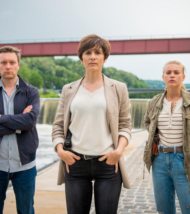 "In Wahrheit – Unter Wasser": Die Ermittler Freddy Breyer (Robin Sondermann), Judith Mohn (Christina Hecke), Lisa (Jeanne Goursaud) alle mit Kamerablick am Flussufer der Nied.