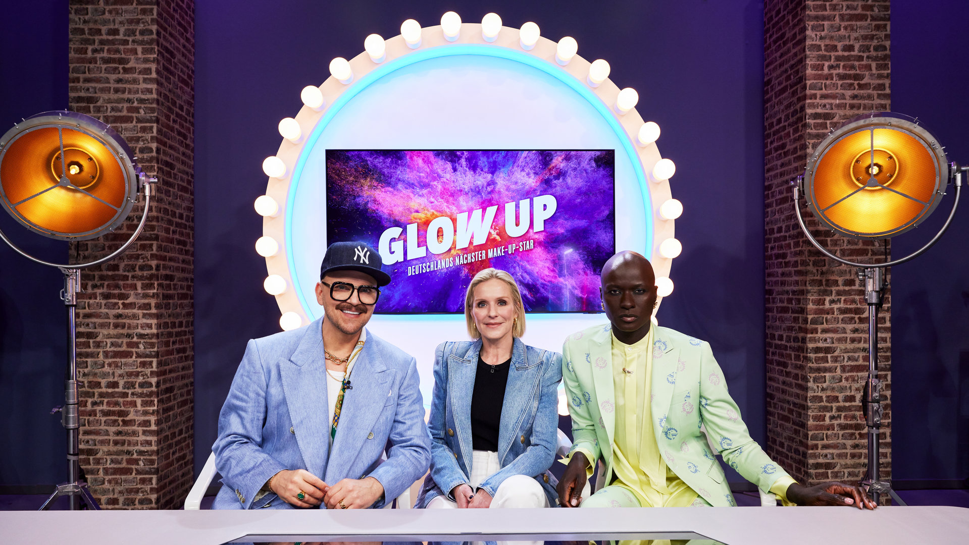 "Glow Up - Deutschlands nächster Make-up-Star": Armin Morbach und Loni Baur posieren mit Gastjuror Papis Loveday am Jury-Tisch im Glow-up-Headquarter.