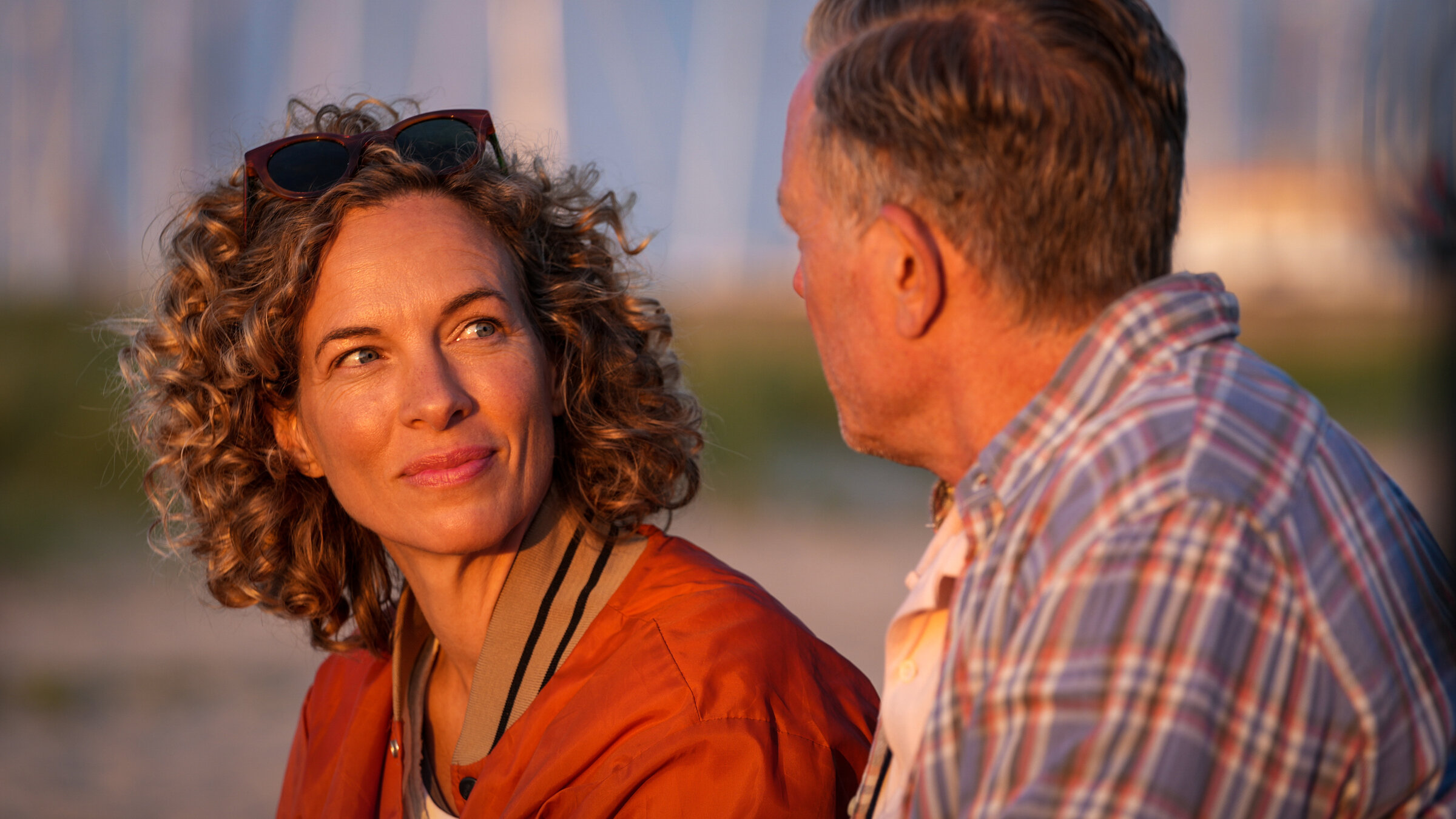 "Dan Sommerdahl – Tödliche Idylle - Rave and Love": Josefine (Maibritt Saerens) und Dan (Peter Mygind) sitzen am Strand, der im Hintergrund, nur verschwommen, liegt. Die beiden sehen sich an. Dan sitzt mit dem Rücken zur Kamera.