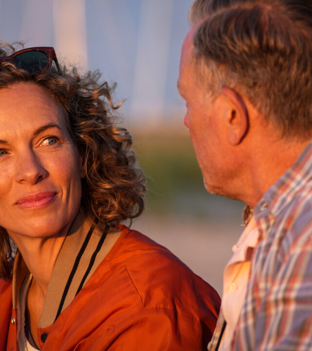 "Dan Sommerdahl – Tödliche Idylle - Rave and Love": Josefine (Maibritt Saerens) und Dan (Peter Mygind) sitzen am Strand, der im Hintergrund, nur verschwommen, liegt. Die beiden sehen sich an. Dan sitzt mit dem Rücken zur Kamera.